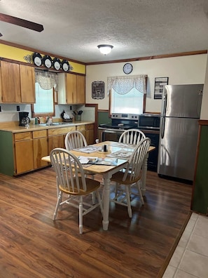 A compact kitchen with wooden cabinets, a stainless steel refrigerator, a stove, and a dining table with four chairs.