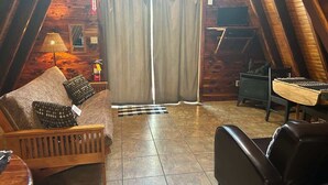 Ein gemütliches Dachzimmer mit Holzbalkendecke, einer Couch mit gemusterten Kissen, einem kleinen Tisch und einem Sessel.