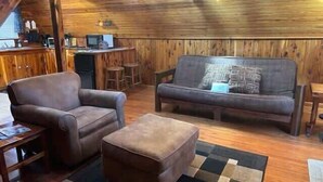 A cozy cabin interior with a wooden ceiling, a sofa, a chair, and a small table.