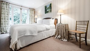 A bedroom with a large bed, two bedside lamps, a chair, and a view of greenery through the window. - 2 Bed 2 Bath Garden Flat in Victoria Pimlico (London)