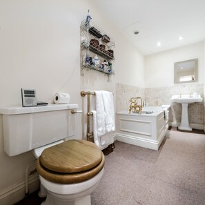 A bathroom with a toilet, a sink, and a bathtub. There is a shelf with toiletries above the toilet.