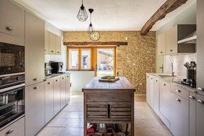A kitchen with stone walls, wooden beams, and a central island.