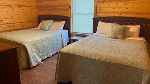 A cabin-style room with two beds, wooden walls, and a window with blinds.