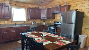 A wooden cabin kitchen with a dining table set for four, equipped with a refrigerator, stove, and sink.