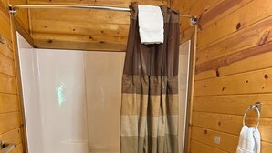 A compact bathroom with a bathtub, toilet, and wooden walls.