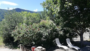 A stone patio with two white lounge chairs, a red pot, and a stone wall. - Maison Le Pijoulet, Dream vacation in Ariege (TIGNAC)