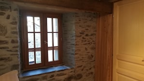 A room with a stone wall, a wooden door, and a window with a view of the outside. - Maison Le Pijoulet, Dream vacation in Ariege (TIGNAC)