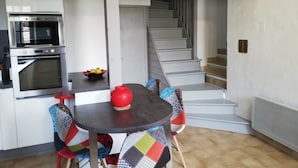 A kitchen with a built-in oven and microwave, a small table with a red pot, and a staircase leading to another level. - Maison Le Pijoulet, Dream vacation in Ariege (TIGNAC)