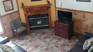 Una sala de estar con chimenea, dos sofás, un televisor y una silla.