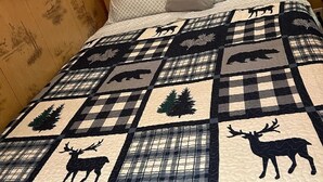 Una cama con colcha que presenta siluetas de animales y un estampado de cuadros.