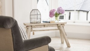 Ett mysigt rum med en träbänk, en svart läderfåtölj, en fågelbur, en bok och en vas med blommor.