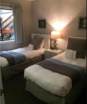 Two single beds with matching headboards and footboards, a bedside table, and a window with a view of an outdoor staircase.