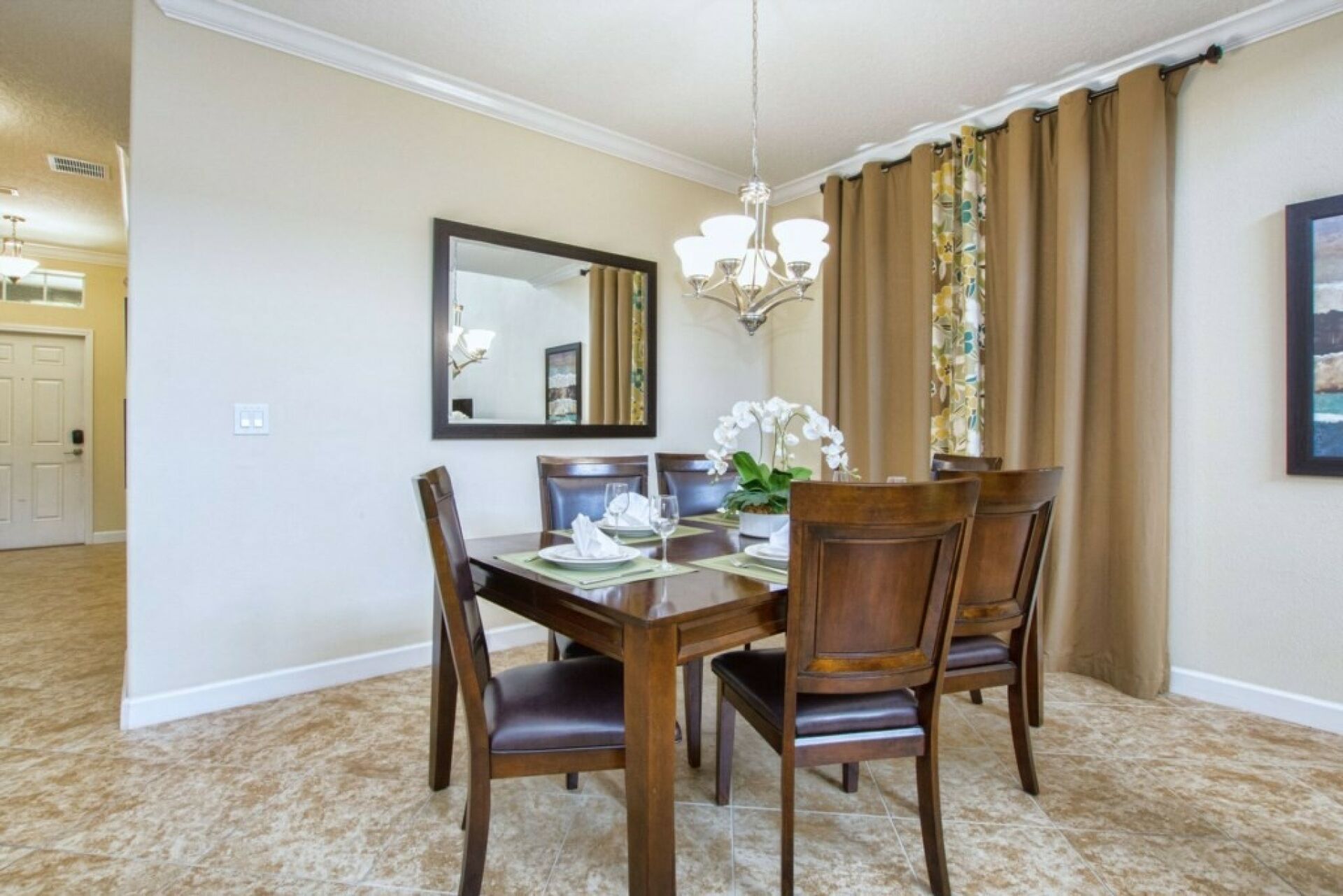 Un coin repas comprenant une table en bois, des chaises, un lustre, un miroir et des rideaux.