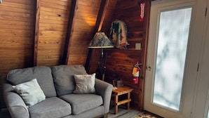 Una habitación acogedora con un sofá gris, una mesita de madera, una lámpara y una puerta con ventanal.