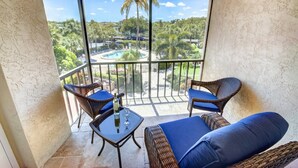 Varanda com móveis de vime, mesa de vidro e vista para uma piscina e vegetação.