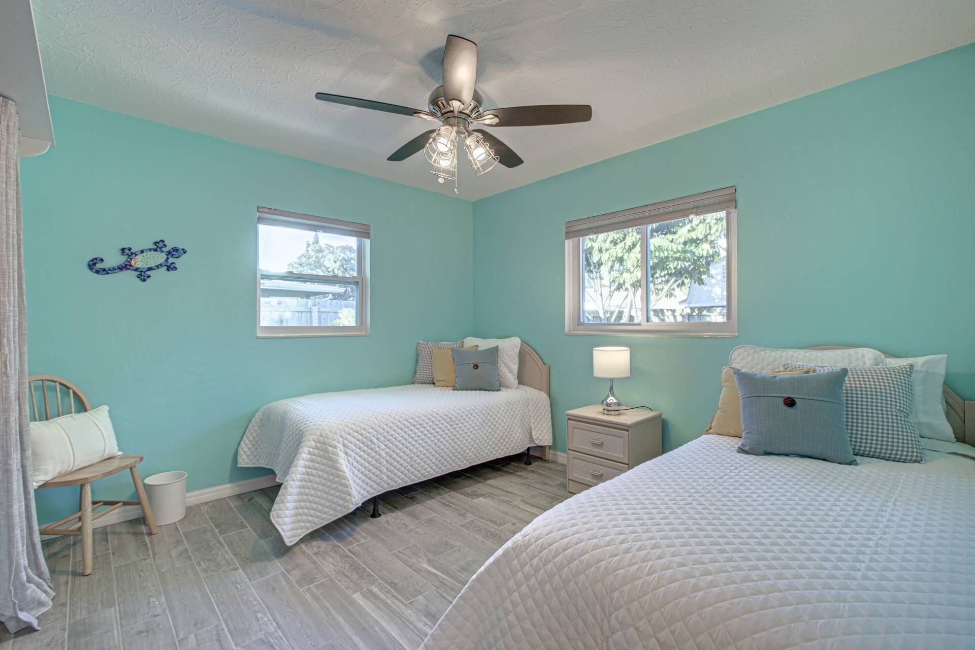 A bedroom with two beds, a ceiling fan, and two windows.