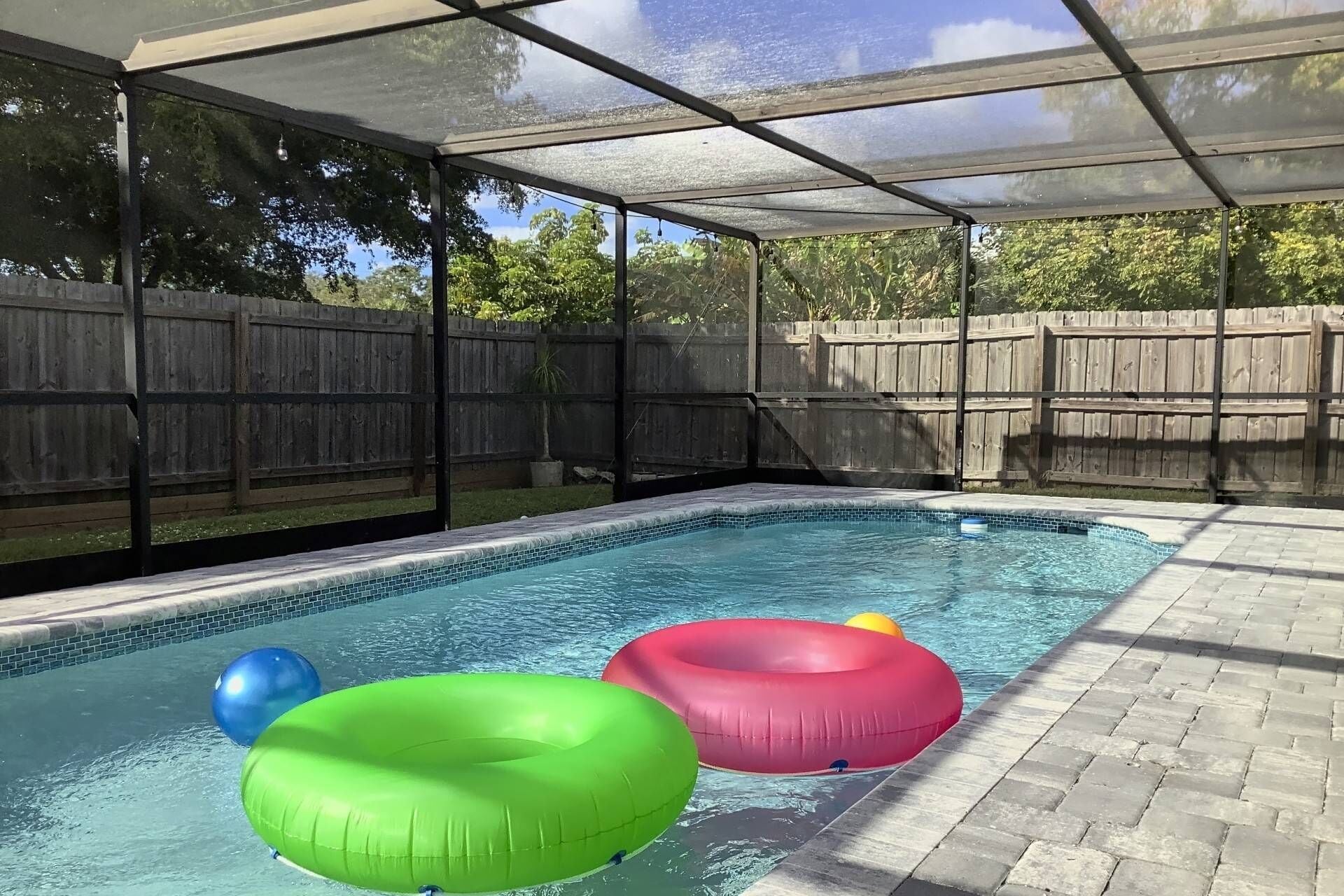 A swimming pool with a glass enclosure, surrounded by a wooden fence and a paved deck.