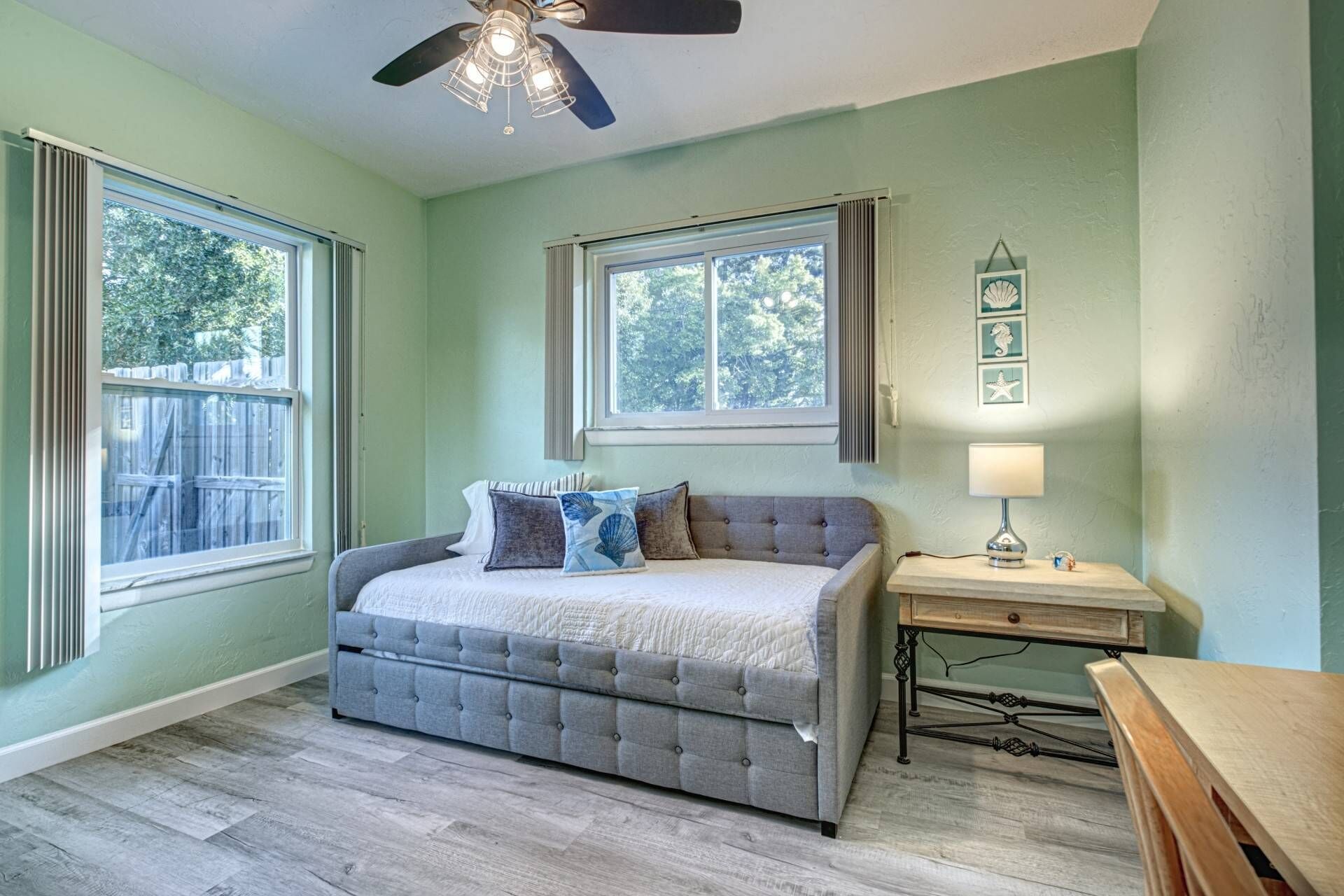 A bedroom with a bed, a ceiling fan, a window, and a bedside table with a lamp.