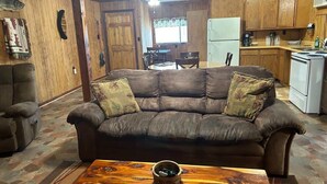 Una sala de estar con un sofá de cuero marrón, una mesa de centro de madera y un comedor con mesa y sillas.