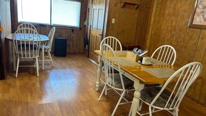 Un comedor con una mesa de madera y sillas blancas, una ventana con persianas, y una puerta.