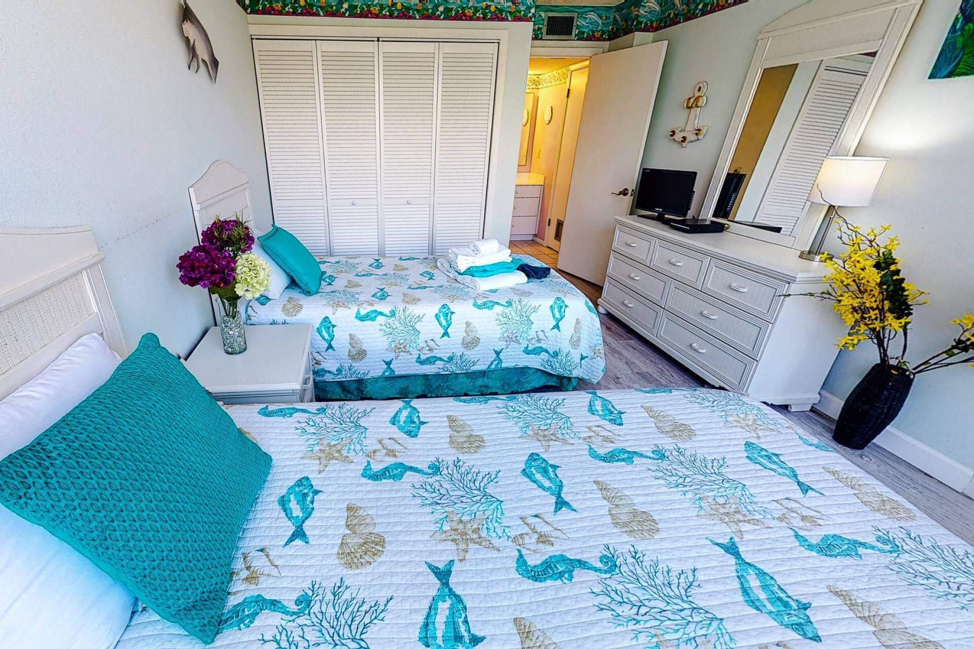 Une chambre avec deux lits, une commode, une télévision et un miroir.