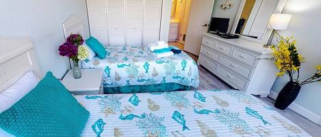 Une chambre avec deux lits, une commode, une télévision et un miroir.