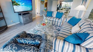 Ein Wohnzimmer mit Fernseher, gestreifter Couch und einem Glastisch.