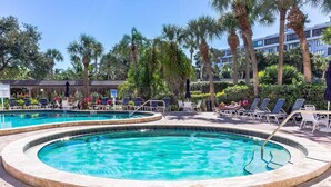 Ein Poolbereich mit zwei runden Pools, umgeben von Liegestühlen und Palmen.