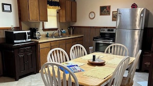 Una cocina con armarios de madera, microondas, refrigerador y una mesa de comedor con sillas.
