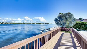 A wooden boardwalk leading to a waterfront area with a boat dock, palm trees, and a clear blue sky. - Harbor Towers 2nd Fl 2 Bedroom Pool View (Siesta Key)
