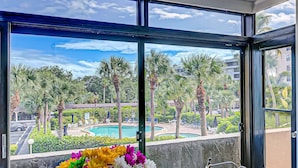 A balcony with a view of a swimming pool, palm trees, and a cityscape. - Harbor Towers 2nd Fl 2 Bedroom Pool View (Siesta Key)