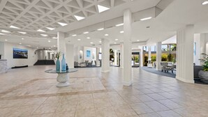 A spacious lobby with a high ceiling, large windows, and a central glass table with decorative items. - Harbor Towers 2nd Fl 2 Bedroom Pool View (Siesta Key)