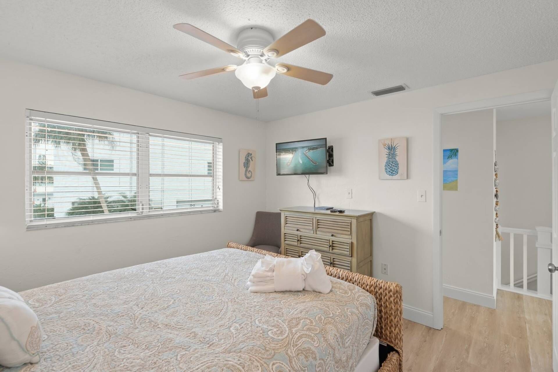 A bedroom with a bed, a ceiling fan, a TV, and artwork on the wall.