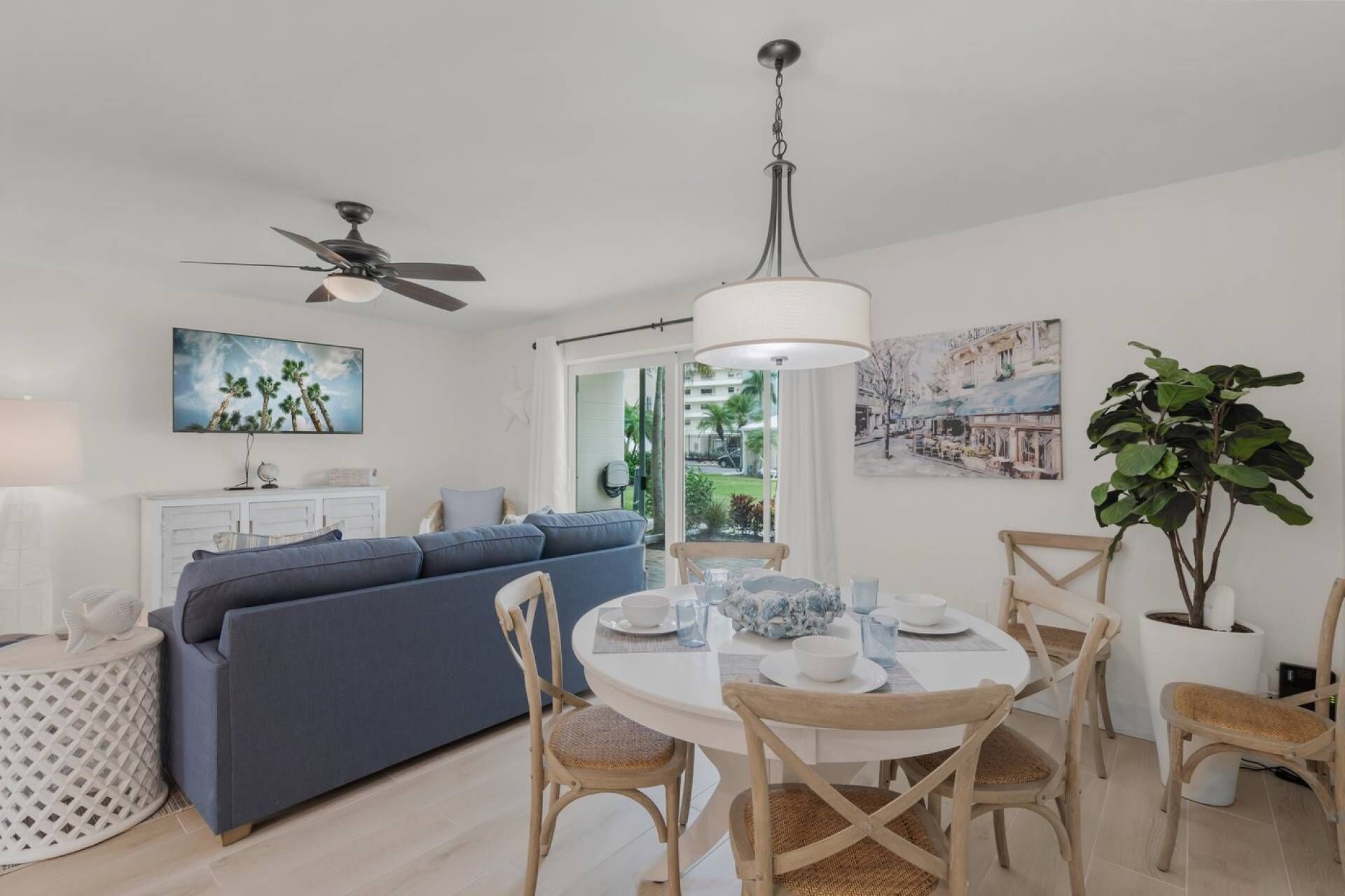 Sala moderna com sofá azul, mesa de jantar posta para quatro pessoas e uma planta grande.