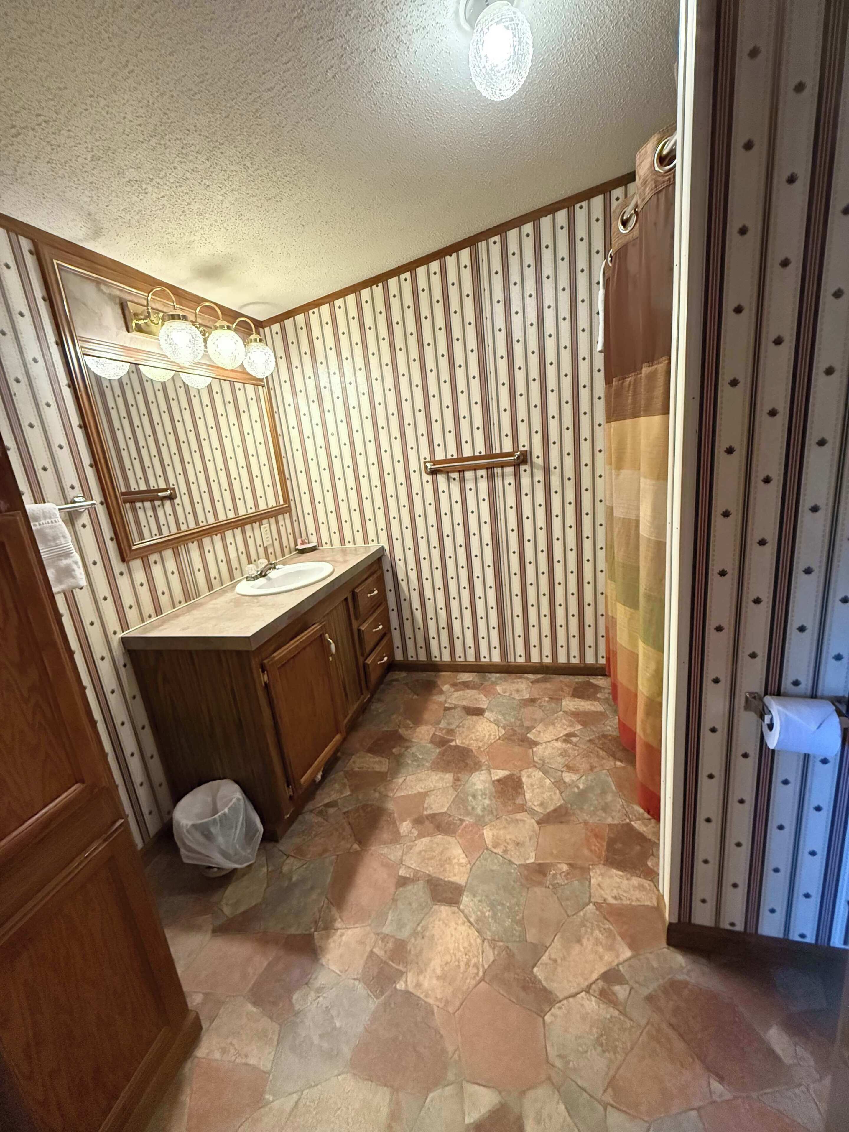 Une salle de bain avec un meuble-lavabo en bois, un miroir, un lavabo, un rideau de douche et un mur à motifs.