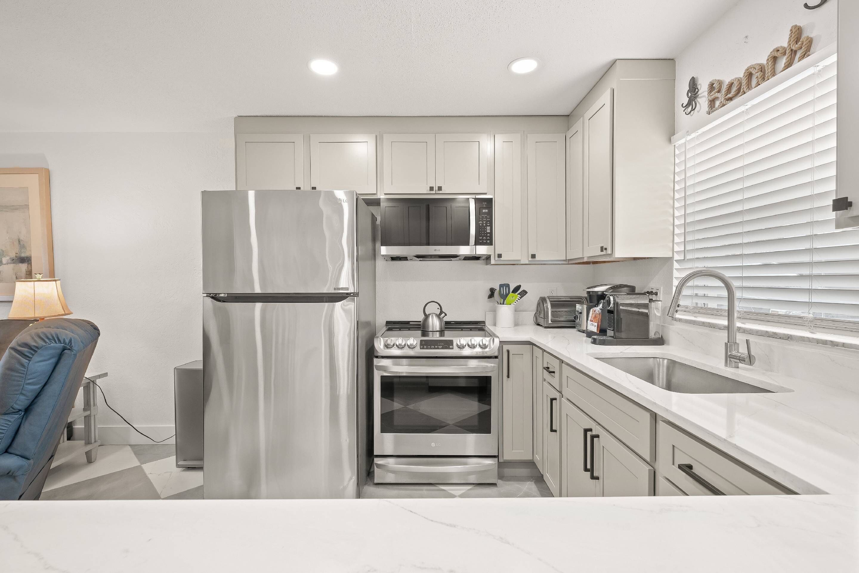 A modern kitchen with stainless steel appliances, white cabinetry, and a marble countertop.