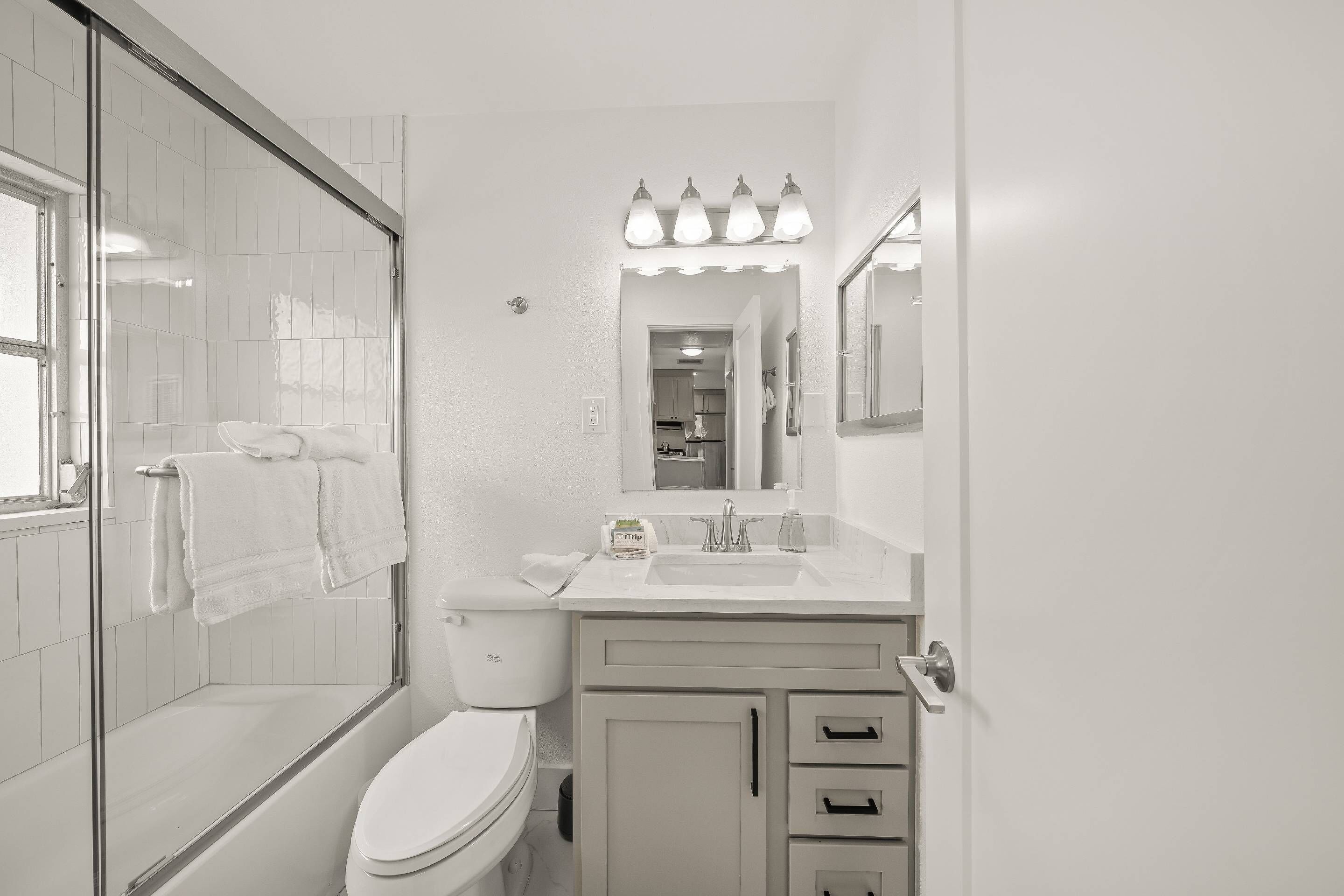 Un baño moderno con cabina de ducha de vidrio, inodoro blanco, lavabo con espejo y mueble con cajones.