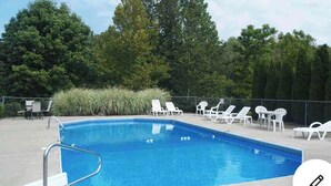 A rectangular swimming pool with a metal ladder, surrounded by white lounge chairs and a grassy area with trees. - Patoka Lake Luxury Home #21 at Patoka 4 Seasons Resort (Eckerty)
