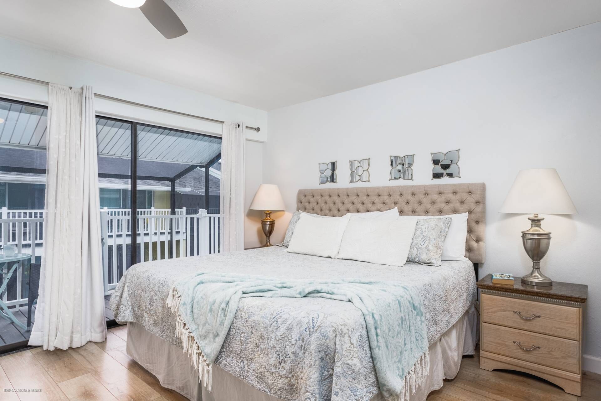 A bedroom with a large bed, two bedside lamps, a wooden nightstand, and a balcony view.