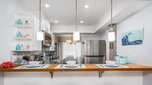 A modern kitchen with white cabinetry, a stainless steel refrigerator, and a dining area with stools. - Key Point Village - Stickney Point (Sarasota)