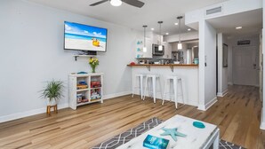 A modern living room with a flat-screen TV, a coffee table with a book, and a ceiling fan. - Key Point Village - Stickney Point (Sarasota)