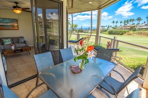 Eine überdachte Terrasse mit einem Glastisch und Stühlen, einer Couch und Blick auf einen Golfplatz.