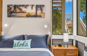 Une chambre à coucher avec un lit, une table de chevet, une lampe et un tableau représentant une scène de plage.