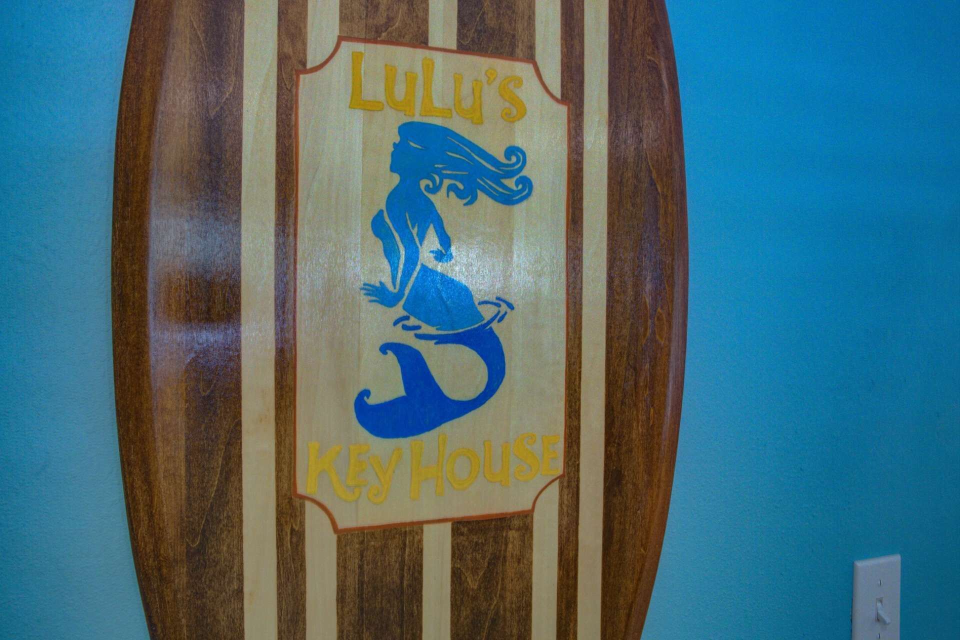 A wooden plaque with a mermaid illustration and the text "Lulu's Key House".
