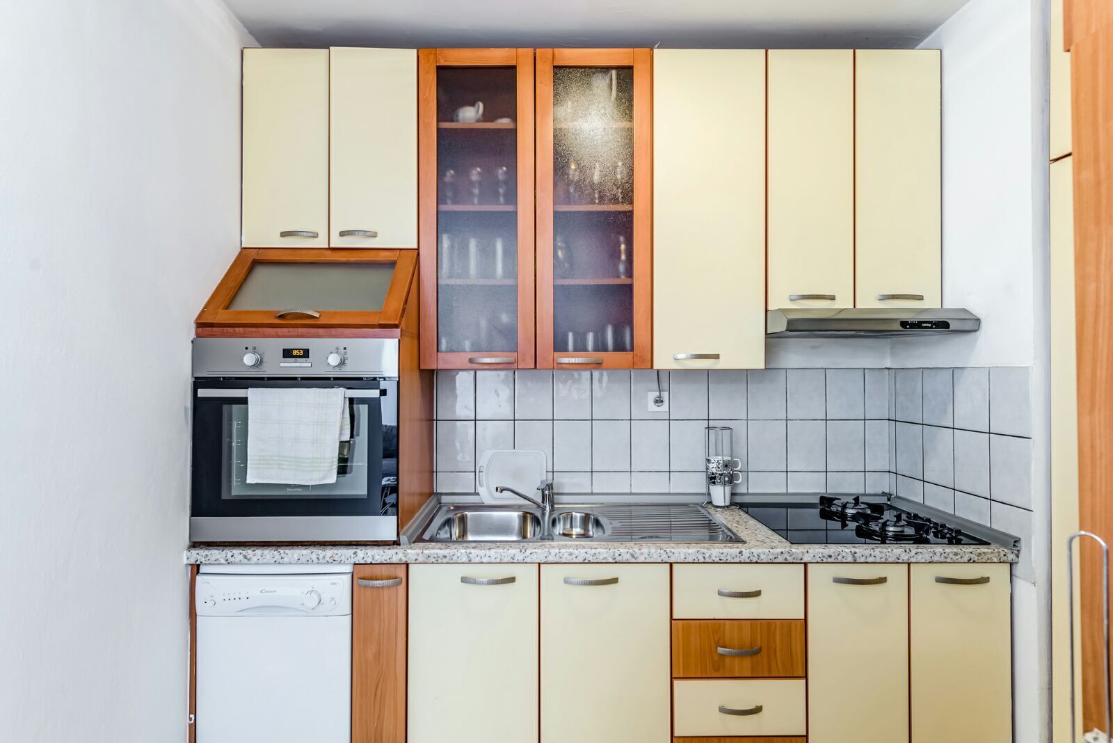 Eine kompakte Küche mit integriertem Backofen, Kochfeld, Spüle und Holzschränken.