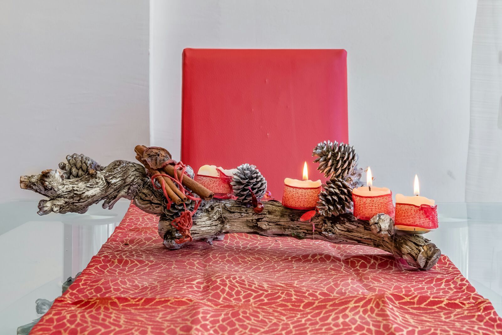 A table with a red patterned tablecloth, a decorative log centerpiece, and three lit candles.