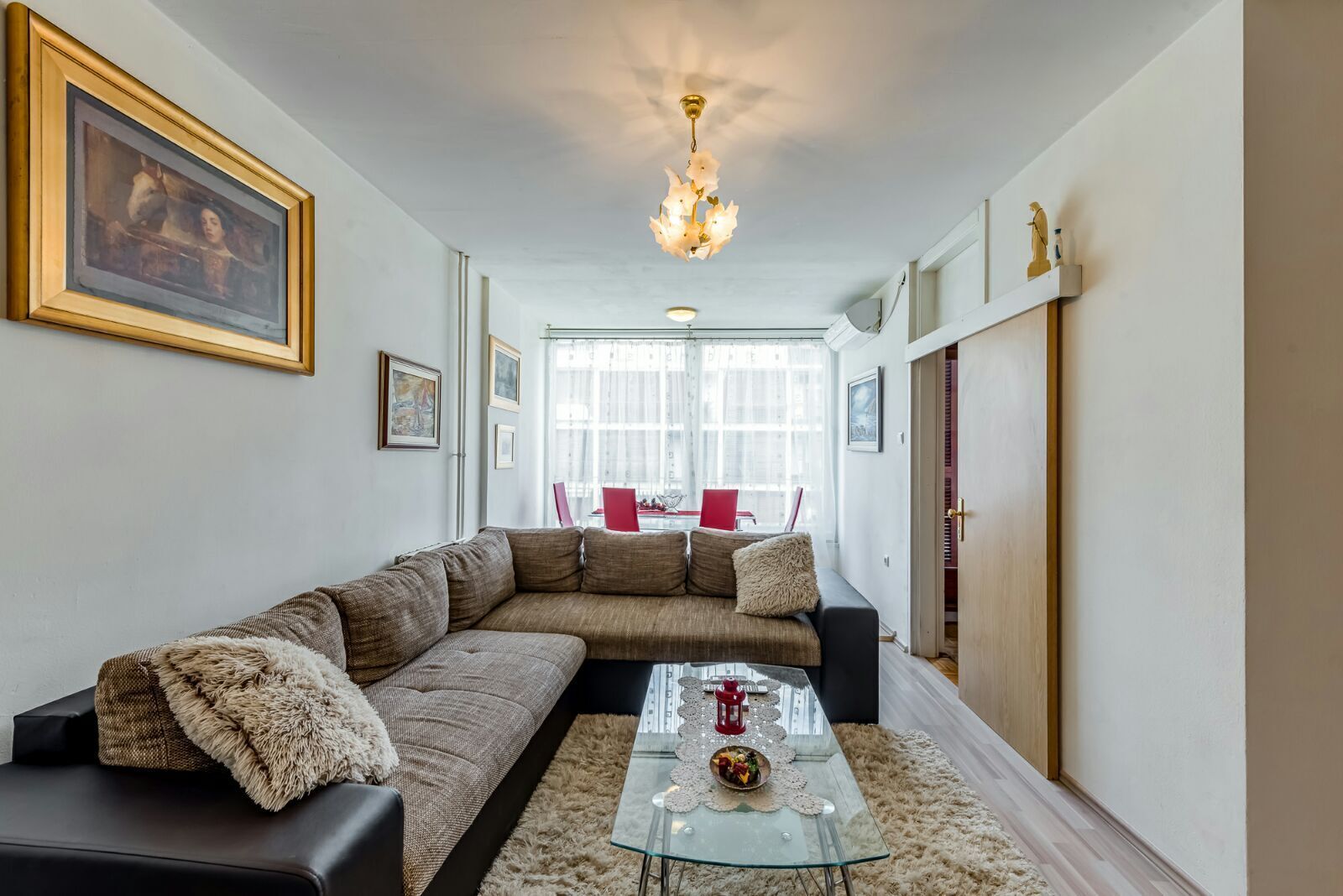 A modern living room with a sectional sofa, a glass coffee table, and a chandelier.