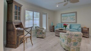 A spacious living room with a wooden cabinet, a floral armchair, a blue sofa, and a ceiling fan. - Lulu's Key House Leatherback 2/2 Downstairs (Siesta Key)