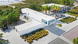 A modern building with a flat roof, large windows, and a covered outdoor area with seating. - Lulu's Key House Leatherback 2/2 Downstairs (Siesta Key)