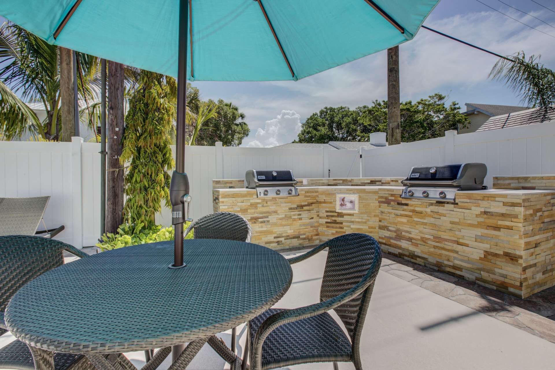 Eine Terrasse im Freien mit einem runden Tisch, Korbstühlen, einem Grill und einer Steinsäule.